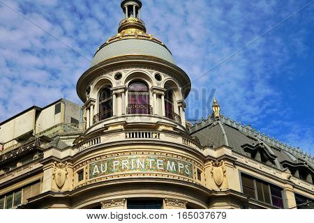 Detail of shopping centre Au Printemps in Paris. Gold dome with blue sky in background. Classical building.
