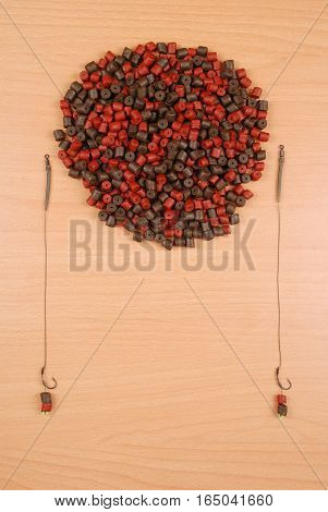 Fishing bait with hook and brown with red pre-drilled halibut pellets for carp fishing isolated on wood background with soft shadow