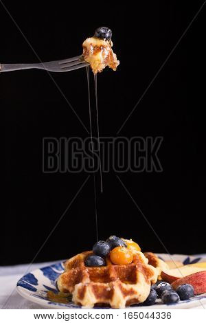 Blueberry waffle set in a nice dish and a fork cut in piece with black background copy space.