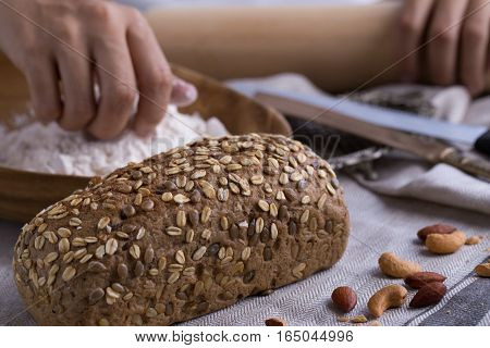 Whole grain bread put on kitchen napkin decorated with almond with a chef holding dough roller at the background.