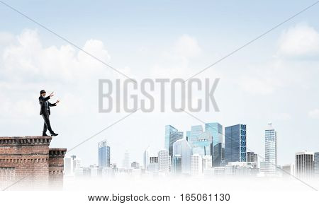 Businessman with blindfolder on eyes walking on building top