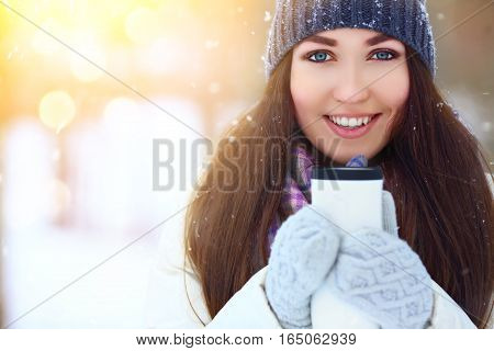 Winter young woman portrait. Beauty Joyful Model Girl holding thermocup and smiling, having fun in winter park. Beautiful young woman laughing outdoors. Enjoying nature, wintertime.