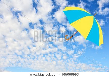 Umbrella in Ukrainian flag colors flies in sky against of pure white clouds.Mary Poppins Umbrella.Wind of change concept.