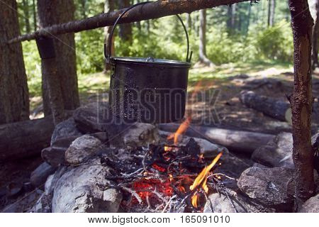 Cauldron boils on the fire in the forest. In marching a saucepan preparing food. Adventure tourism, camping, cooking on a fire. Survival in the forest. Stalker