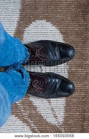 Close up men wear blue jean and brown leather shoes on floor.