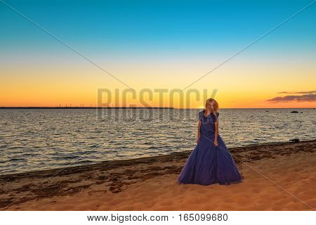 Beautiful girl in a bright violet dress by the sea. Against the background of the summer lanshaft. Young romantic woman in the sunshine, sunset.