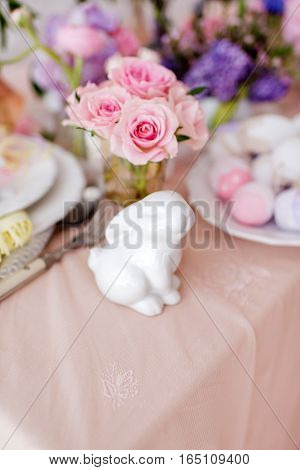 on the table with a pink tablecloth vase with flowers and white porcelain rabbit