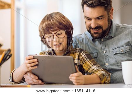 Do like this. Father and son sitting at table, speaking about something while playing games