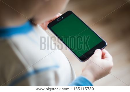 The child is holding a phone in his hand with a green screen for chroma keyer