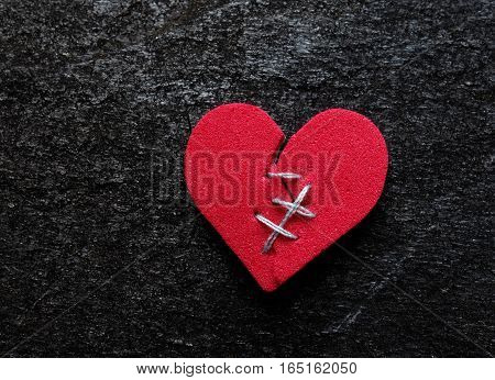 Red broken heart with thread stitches on dark background