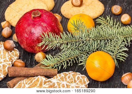 Pomegranate with cookies cinnamon tangerine and branch of christmas tree on the tabke. Christmas decoration.