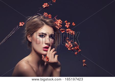 Beautiful young woman with make-up and loose hairdo holding artificial sakura branch with orange flowers. Beauty shot on dark background. Copy space.