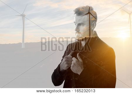 Double exposure portrait of a businessman thinking about renewable electricity combinated with sunset landscape and winmills