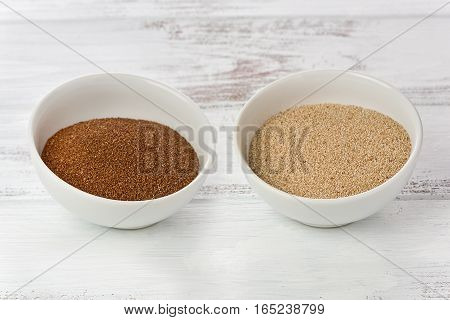 Two small bowls with ethiopian teff grains on a painted wood background. One bowl has brown teff grains and the other has white teff grains.