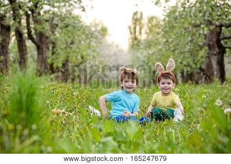 Two Little Kids Boys And Friends In Easter Bunny Ears During Traditional Egg Hunt In Spring Garden,