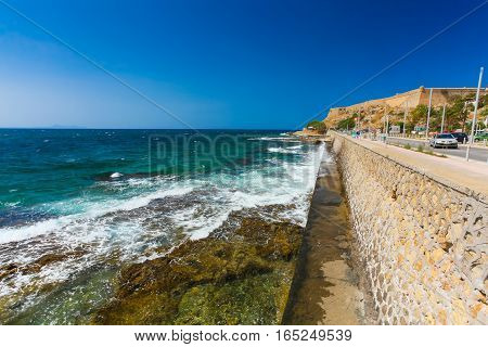 Rethymnon Island Crete Greece - July 1 2016: People are walking on Leoforos Emmanouil Kefalogianni embankment and watching on the sea with clear emerald water and sharp underwater stones.