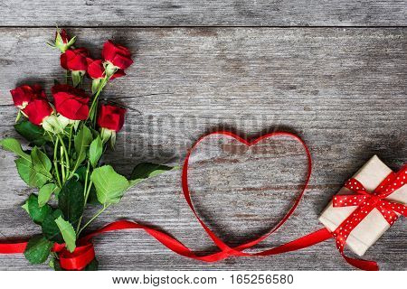 bouquet of red roses and heart shaped red ribbon with gift box on rustic wooden background. valentines day greeting card