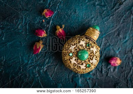 Small Vintage ornate perfume bottle and dry buds of a rose on a dark blue background