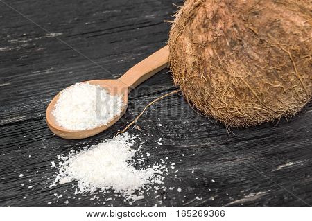 Coconut shaving in a wooden spoon and coconut on black wooden table.