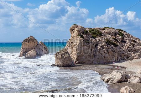 Aphrodite's Rock in Cyprus. Taken on a bright summer's day with rough seas and has some people on the beach giving scale.