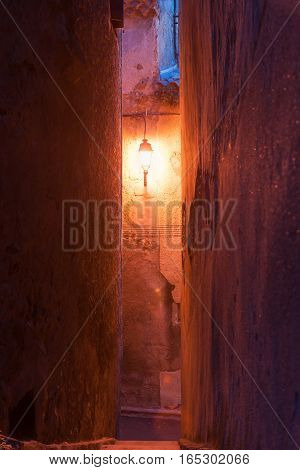 Warm glow of single street light at end of small Frech town narrow street between high walls of traditional architecture