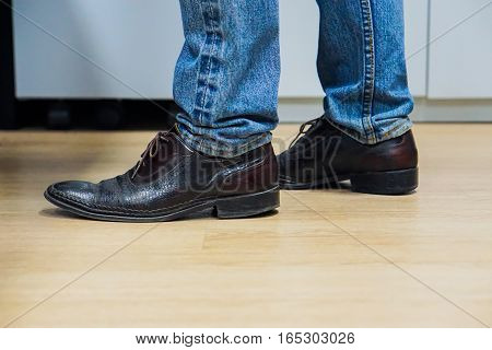 Close up men wear blue jean and brown leather shoes on floor.