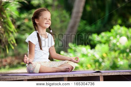 Child doing exercise on wooden platform outdoors. Healthy lifestyle. Yoga girl