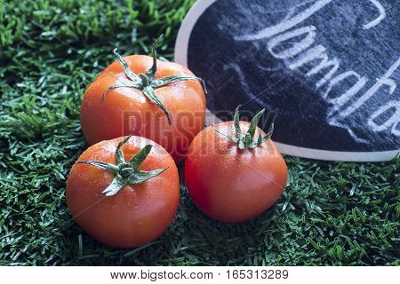 closeup of three red tomato with grass background and black sign