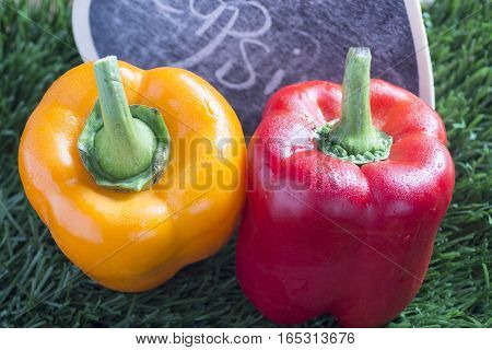 closeup of two paprikas yellow and red on grass background