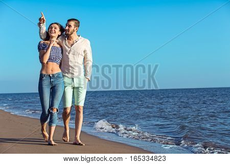 Couple walking on beach. Young happy interracial couple walking on beach smiling holding around each other. Latino woman, Caucasian man.