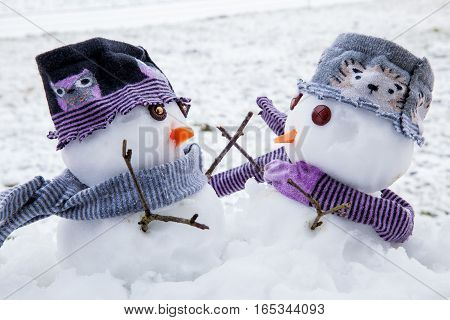 Two cute snowmen dressed for winter in scarfs and hats embracing each other as long lost friends. Winter scene with snow.