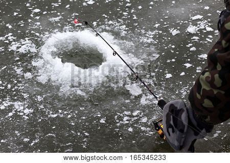 A hole in ice and fishing rod in the hand of fisherman
