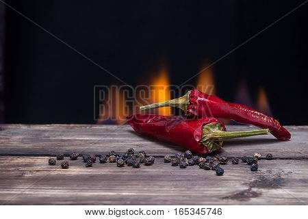 Red peppers chilli with round flavoring on the wooden table and fire on the background