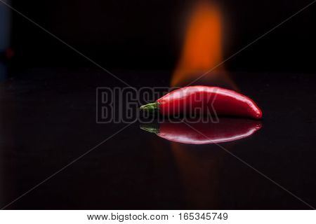 Red peppers chilli on the glass table with reflection and fire on the black background