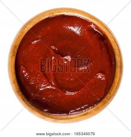 Tomato ketchup in wooden bowl. Also called catsup or ketsup, is a red table sauce made from tomatoes, often used as a condiment. Isolated macro food photo close up from above on white background.