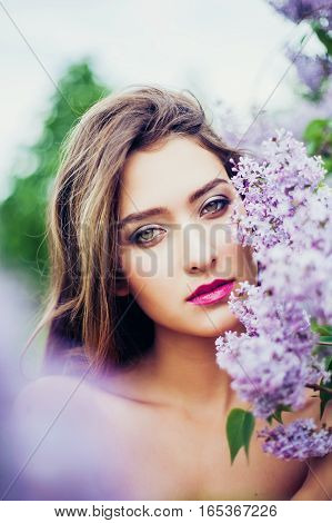Portrait of young beautiful woman posing among lilac flowers. Professional make-up and hairstyle. Perfect skin. Fashion photo. Natural beauty. Springtime.