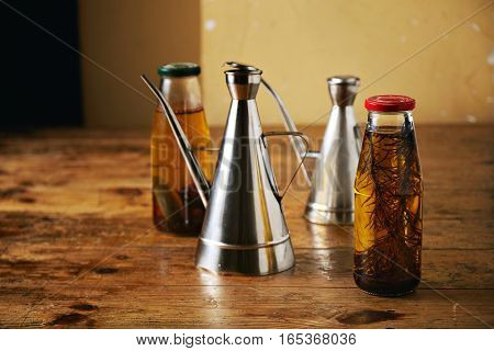 Two bottles with artisan home made spicy olive oil with rosemary and peppers and two shiny metal cruets on a rough brown table