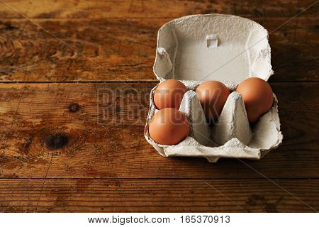 Presentation of opened recyclable egg carton for six eggs containing four big ecological eggs on a aged vintage rustic brown wooden table