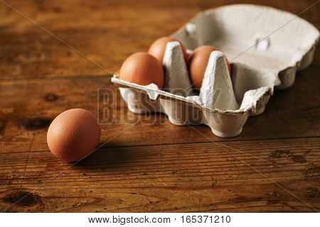 Close up shot of an open recyclable egg carton with 3 eggs inside and one egg next to it on a brown grainy wooden table Ecological healthy food from bio farms.