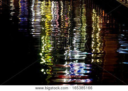 the reflection of light waves in the water Colored city lights reflected on water surface in night.