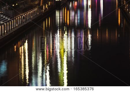 the reflection of light waves in the water Colored city lights reflected on water surface in night.