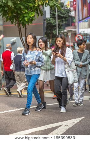 Hong Kong, China - December 6, 2016: asian young women walking talking at their mobile phone in Jardine's Crescent street market of Causaway Bay, on background luxury shops of famous brends.