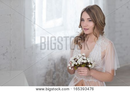 Bride's morning in a bright room. Young sensual woman holds a delicate bouquet of flowers.
