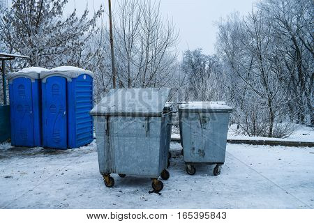 Garbage bins and toilet cubicles in the background Winter Park trees snow cold