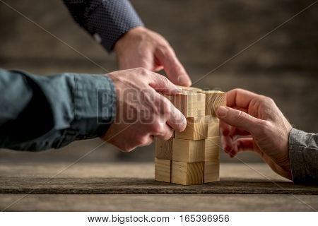 Hands of three people building a tower of wood blocks on a table teamwork concept.