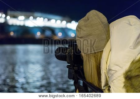 Young girl taking night view photos using DSLR and tripod on urban river bank. Girl night photography.