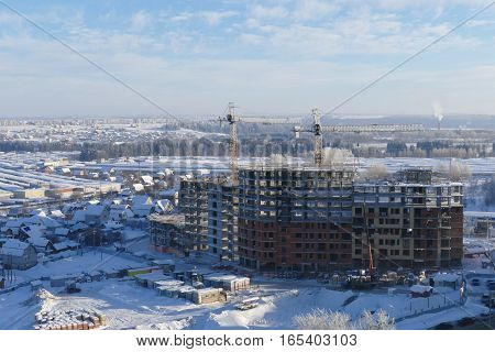Large apartment buildings construction in new district among rural houses, urbanisation in action. Winter season