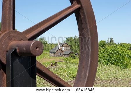 Old abandoned house viewed through a section of a rusty wheel. Selective focus on the house. Part of an abandoned copper mine that is now a Historic National Park in Upper Michigan.