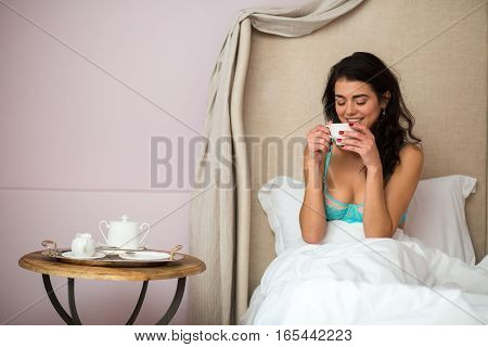 Woman in bed with cup. Young female indoor. My morning starts from coffee.