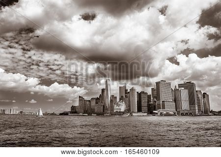 A small sailboat is cruising in New York harbor with the office buildings of lower Manhattan in the background.